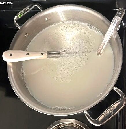 Milk heating on the stove with a whisk and thermometer.